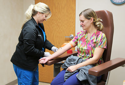Patient sitting in medical chair receiving a blood draw from a nurse.